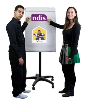 Two friendly looking presenters standing near an information board which had info about the NDIS and group homes on it.