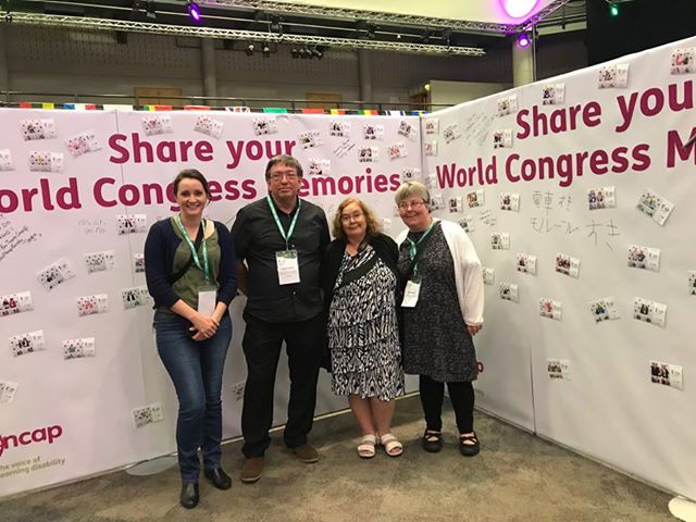 VALID staff members and Judy Huett from Speak Out Tasmania standing in front of Inclusion International World Congress banner
