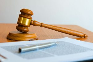A wooden gavel sitting next to a sheaf of documents with a silver pen on it.