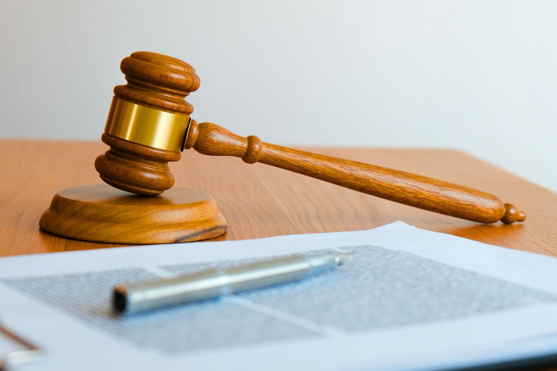 A wooden gavel sitting next to a sheaf of documents with a silver pen on it.